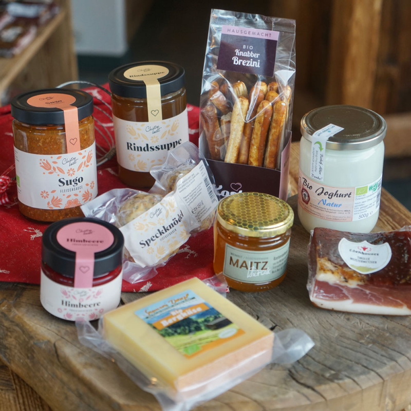 Sortiment regionaler Spezialitäten mit Sugo, Rindssuppe, Bio-Joghurt, Käse, Marmelade, Honig und Speck auf Holztisch